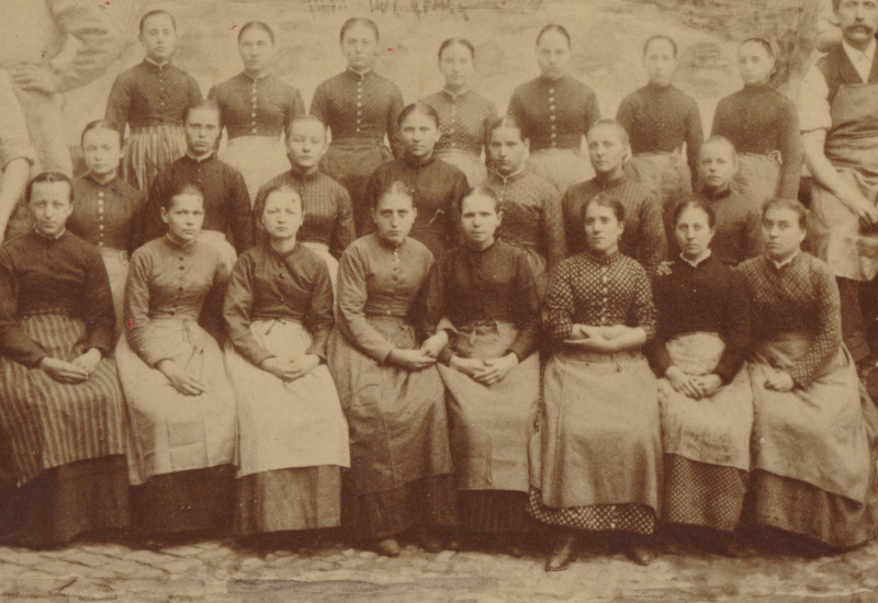 altes Foto, auf dem ca. 20 Frauen in Arbeitskleidung zu sehen sind