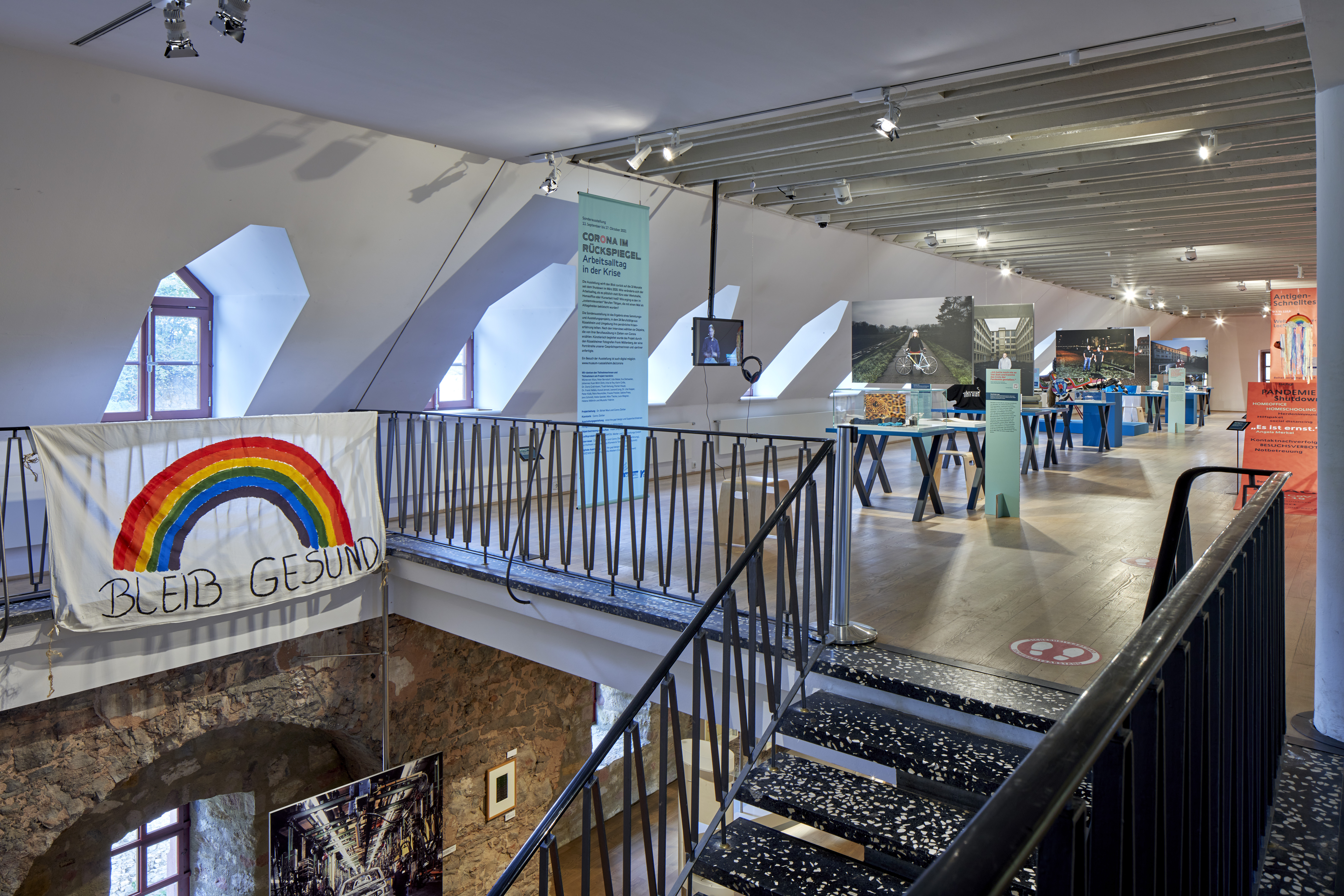 Blick in die Ausstellung "Corona im Rückspiegel"; Banner mit einem gemalten Regenbogen, darunter die Aufschrift "Bleibt gesund!"