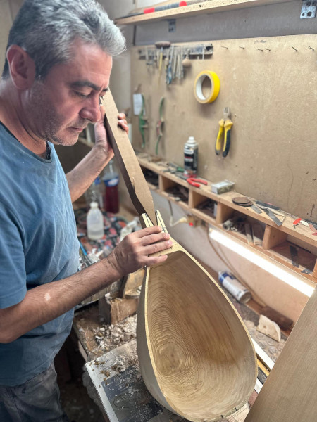 Ein Mann arbeitet an einer Werkbank an einem Instrument aus Holz.