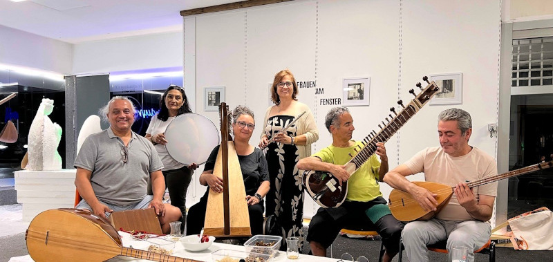 Musiker und Musikerinnen mit unterschiedlichen Istrumenten lächeln auf einem Gruppenfoto.