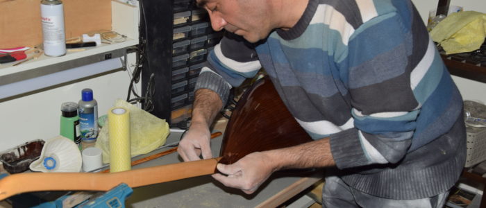 Ein Mann arbeitet an einer Werkbank an einem Instrument aus Holz.